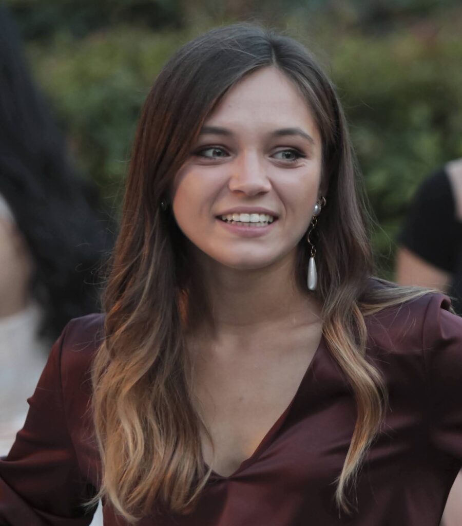 Avv. Irina Carnat sorridente a mezzobusto su uno sfondo sfuocato in ambiente esterno
